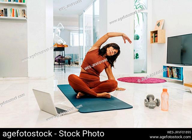 Active woman practicing yoga while E-learning through laptop at home