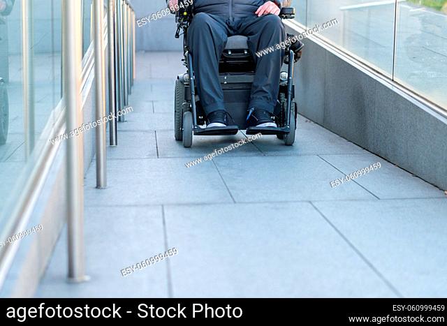 Man in a wheelchair using a ramp next to stairs