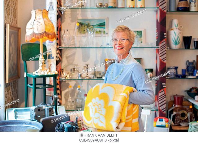 Portrait of mature woman folding yellow blanket in vintage shop