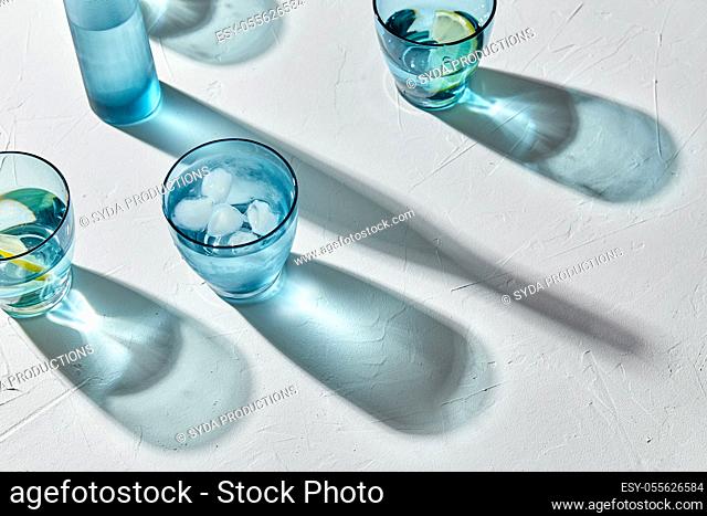 glasses with water and lemons on white background