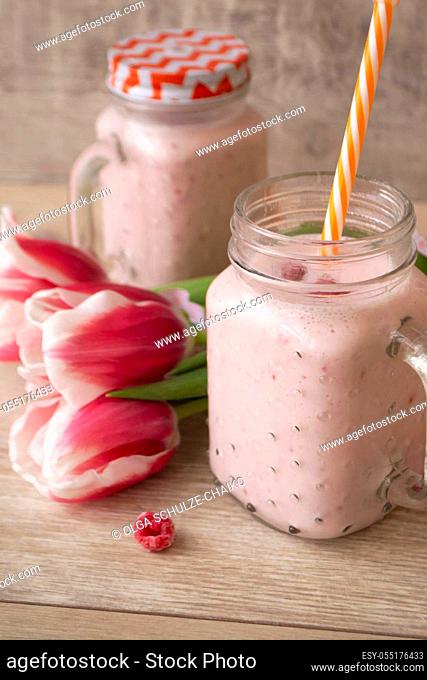 Pink raspberry cream smoothie in mason jar and tulips, vertical