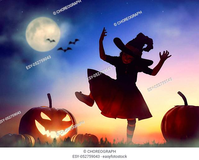 Happy Halloween! Cute little witch with a big pumpkin. Beautiful young child girl in witch costume outdoors