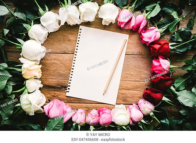 Colorful roses lined up on a wooden floor paper and pencil with space for writing your message
