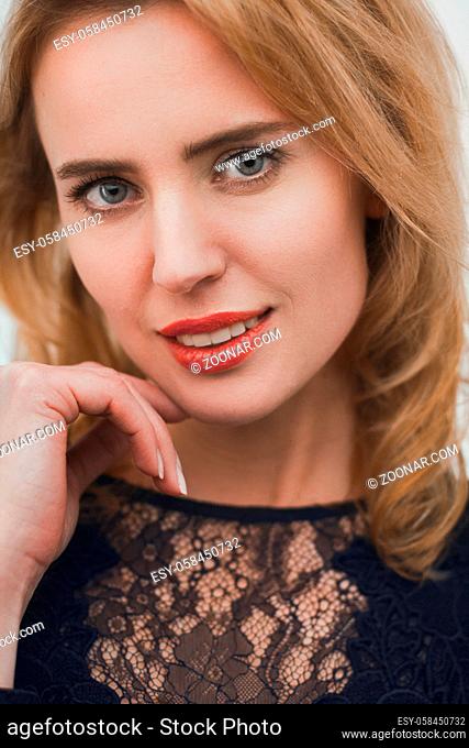 Close up portrait of gorgeous blonde female. Seductive young lady looking straight into camera smiling with her hand near her face
