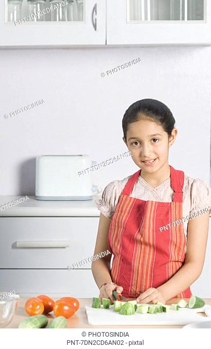Portrait of a girl cutting cucumber with a knife in a domestic kitchen