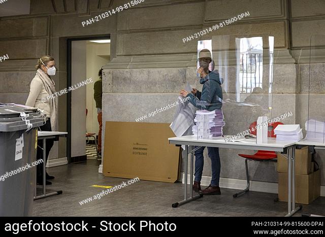 14 March 2021, Hessen, Frankfurt/Main: Voting in the polling station in the Textor School takes place under the observation of a hygienist (l)