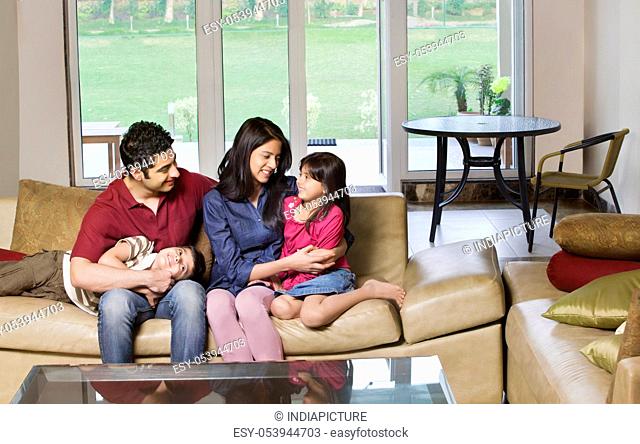 Happy young couple sitting with kids on sofa at home