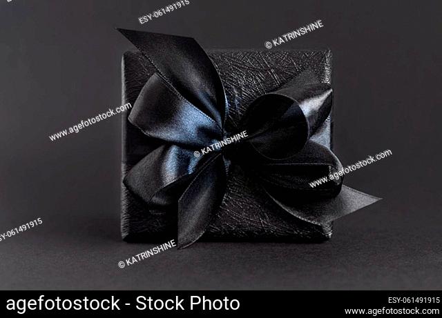 Black Gift Box with a ribbon bow close up on black. Wrapped present for Dark themed Party, Christmas, Birthday, Anniversary. Black Friday concept