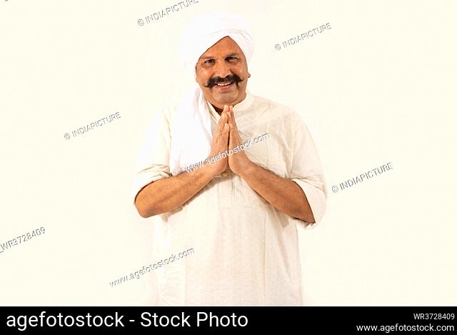A TURBANED VILLAGER SMILING AT CAMERA AND GREEETING WITH FOLDED HANDS