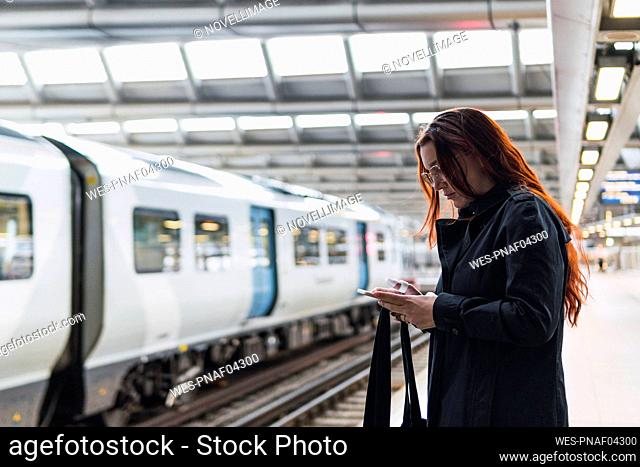 Redhead woman using smart phone at railroad station platform