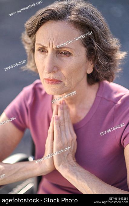 Praying. Serious stressed woman holding hands in praying gesture