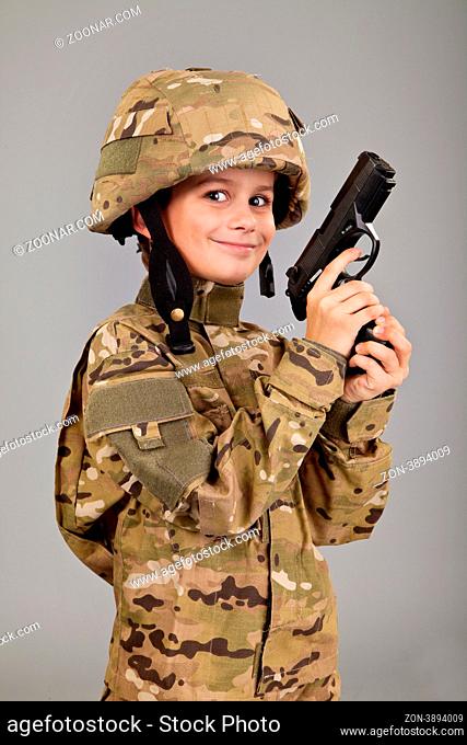 Young boy dressed like a soldier with a gun isolated on gray background