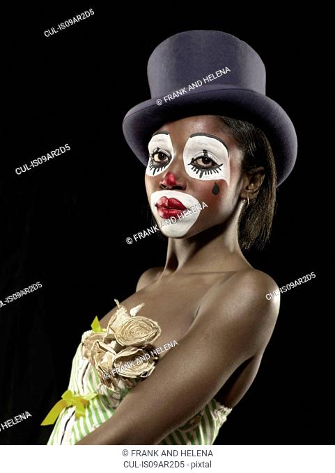 Studio portrait of young woman in clown face paint wearing top hat