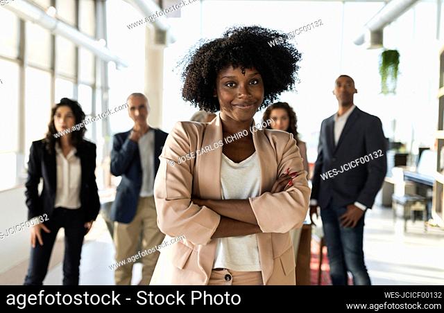 Businesswoman with arms crossed standing with colleagues at office