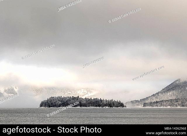 The small island of Sassau in Walchensee in the Byrian Alps covered with snow with clouds in winter