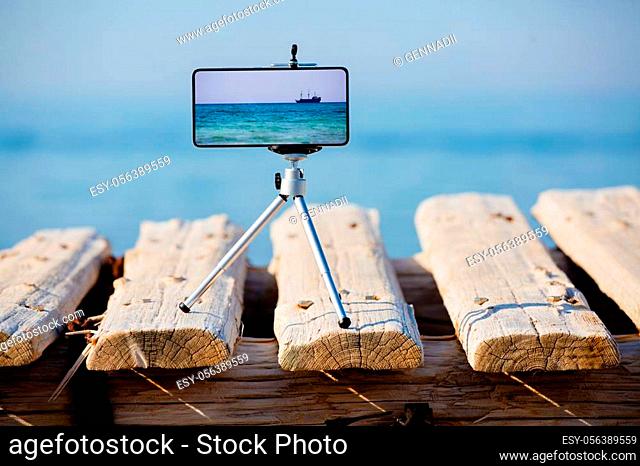 Smartphone with good zoom on tripod making photo and video of beautiful sea landscape with a ship