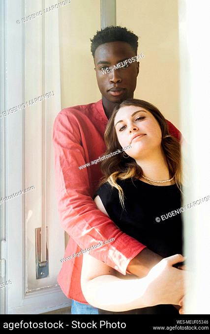 Multiracial couple standing by window at home