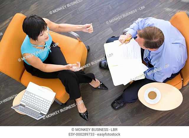 Two businesspeople sitting indoors with coffee laptop and folder
