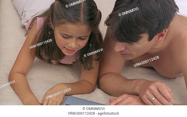 Father and daughter looking at laptop lying down on bed