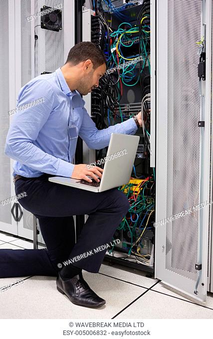 Man fixing wires while doing maintenance with laptop in data center