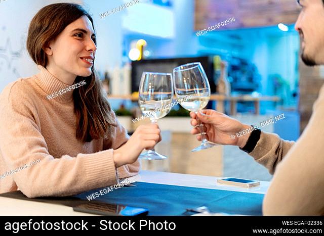 Boyfriend and girlfriend toasting glasses while looking at each other in restaurant