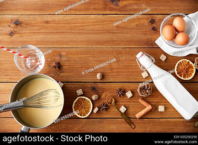 pot with eggnog, ingredients and spices on wood