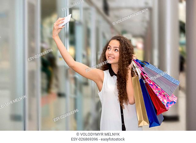 beautiful young woman goes shopping using a smartphone with a shopping bags in the mall