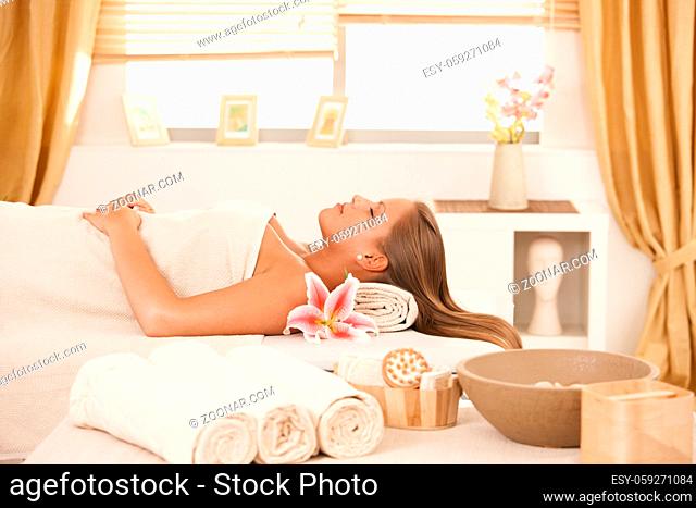Attractive young woman resting with eyes closed on massage bed at spa