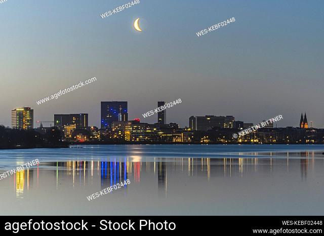 Germany, Hamburg, Moon rises over Outer Alster Lake with city skyline in background