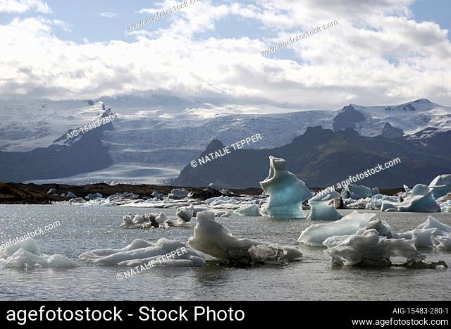 A stunning landscape of a lagoon in Iceland, with the ice cold water and small icebergs, and snowy mountains in the background