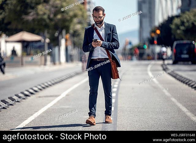 Male business professional using mobile phone while walking in city