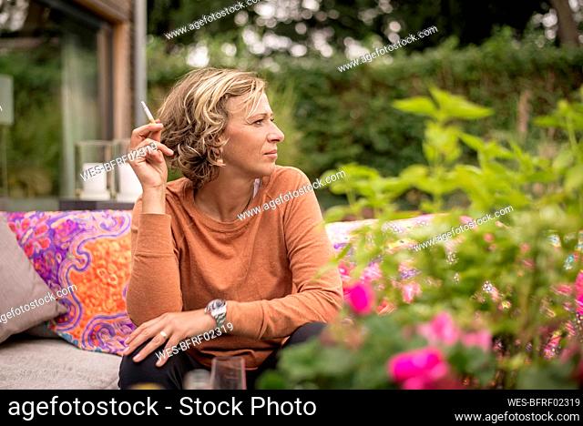 Woman holding cigarette while sitting on sofa at backyard