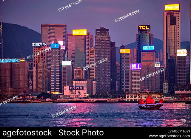 HONG KONG, CHINA - MAY 1, 2018: Tourist junk boat ferry with red sails and Hong Kong skyline cityscape downtown skyscrapers over Victoria Harbour in the evening