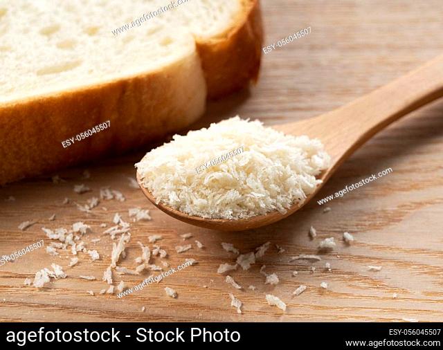 Crumbs and bread in a wooden spoon set against a wooden background
