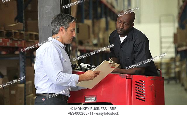 Manger shows fork lift truck driver clipboard with document which they discuss.Shot on Canon 5d Mk2 with a frame rate of 30fps
