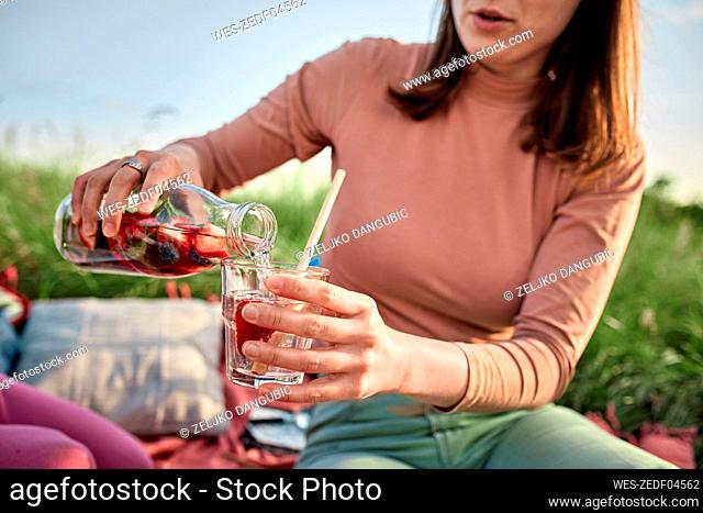 Young woman pouring infused water in glass at field on weekend