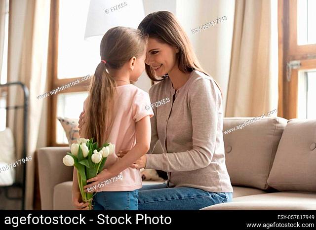 Little kid daughter holding white tulips flowers behind back prepared present congratulating happy mom with mothers day birthday