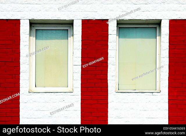 texture of bright red brick wall with white stripes and windows on a sunny day