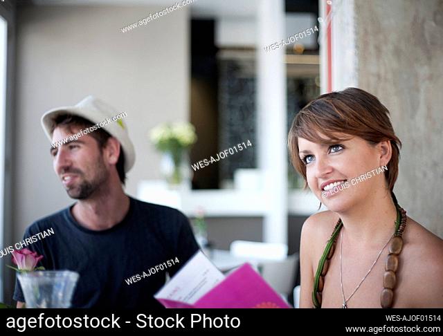 Young woman with menu while sitting by male friend at restaurant