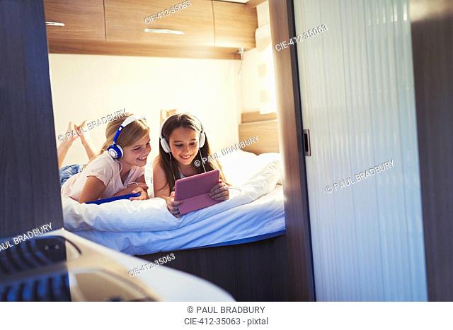 Sisters with headphones sharing digital tablet, watching video inside motor home