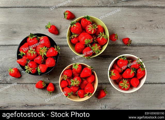 Tabletop view - strawberries in small ceramic bowls, some of them spilled on gray wood desk