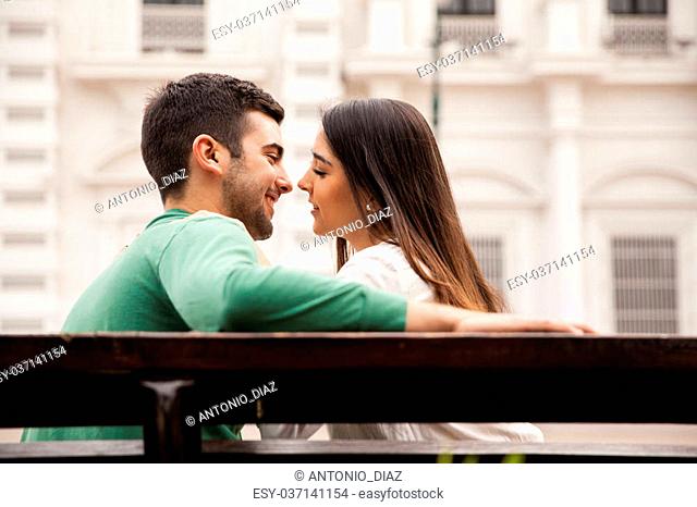 Rear view of a young couple in love sitting on a park bench and about to kiss
