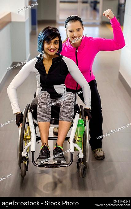 A paraplegic woman and her trainer pose for the camera while in a hallway in a recreational facility: Sherwood Park, Alberta, Canada