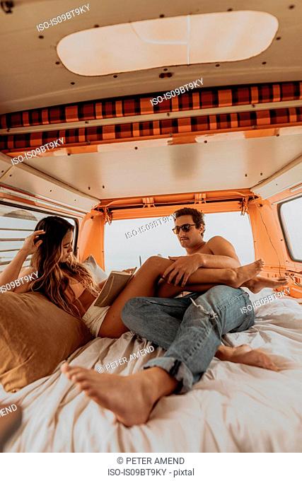 Young surfing couple reclining in back of recreational vehicle at beach, Jalama, California, USA