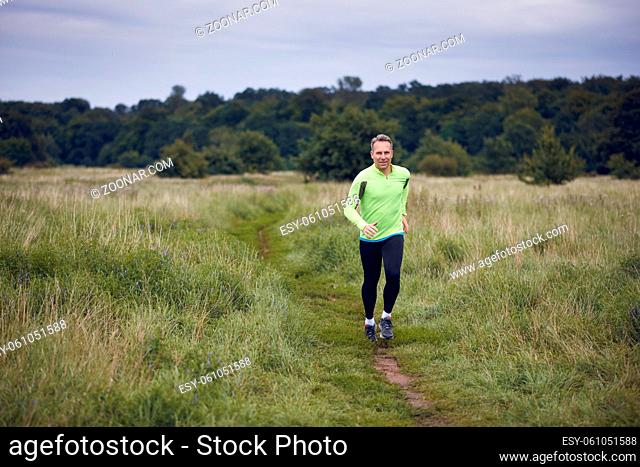 Fit muscular man jogging on a rural trail through grassland wearing sportswear in an active lifestyle concept