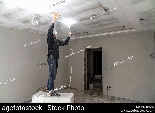 sanding a plasterboard ceiling in a new building with a trowel. High quality photo