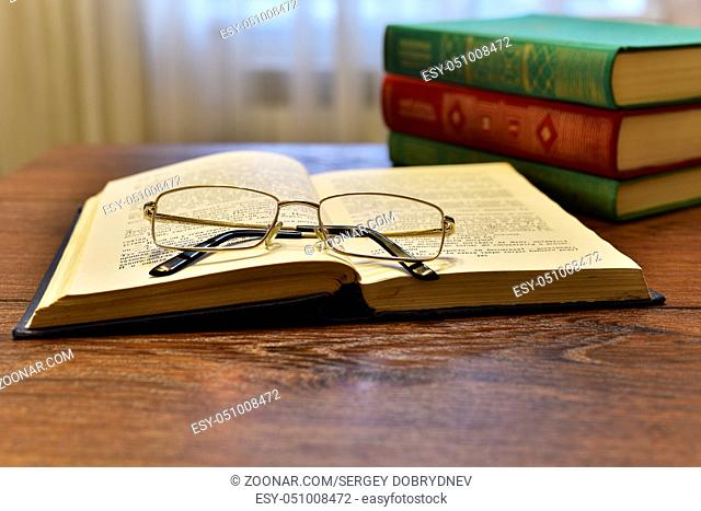 Open book with glasses and stack of books on the table