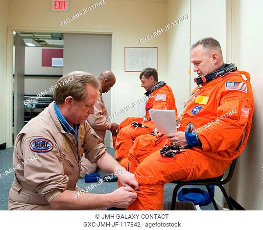NASA astronauts Doug Hurley (right foreground), STS-135 pilot; and Chris Ferguson, commander, don training versions of their shuttle launch and entry suits in...
