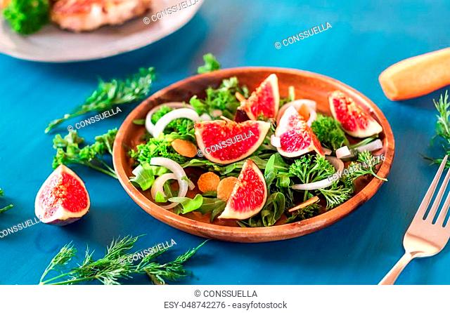 Autumn salad of arugula, figs in brown earthenware plate on a blue background. top view