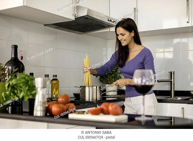Young woman cooking spaghetti in kitchen